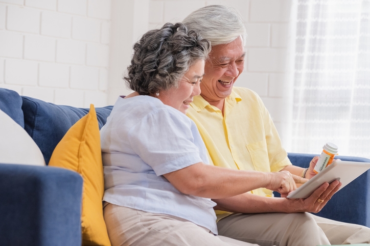 Smiling older Asian couple doing a telehealth visit on their couch